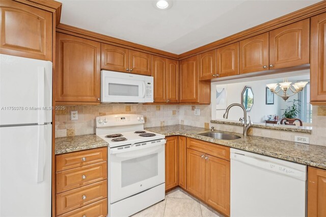 kitchen featuring brown cabinetry, a sink, white appliances, and light stone countertops