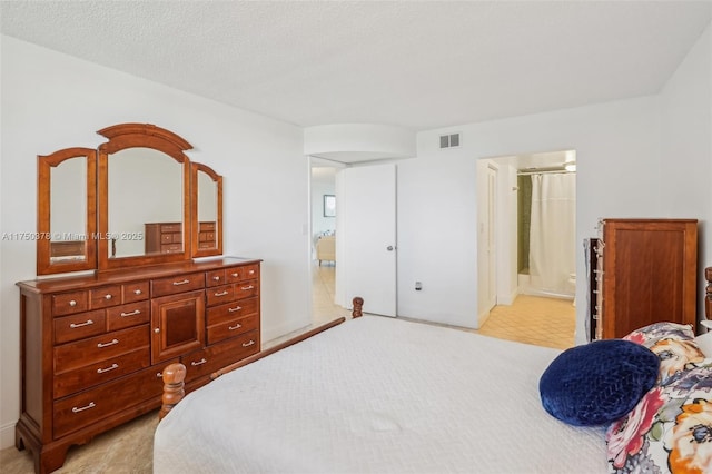 bedroom with connected bathroom, visible vents, a textured ceiling, and light colored carpet