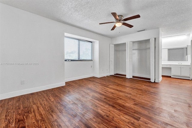 unfurnished bedroom with a textured ceiling, two closets, baseboards, and wood finished floors