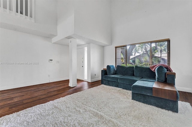 living area with dark wood finished floors, a towering ceiling, and baseboards