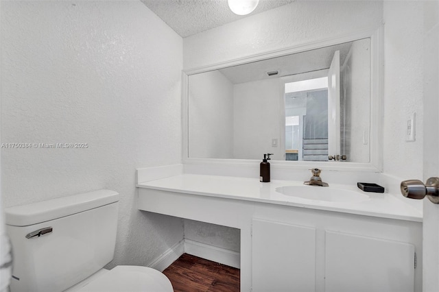 bathroom with a textured wall, toilet, vanity, a textured ceiling, and wood finished floors