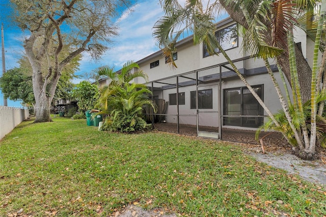 back of property featuring glass enclosure, a yard, fence, and stucco siding