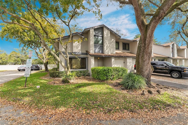 multi unit property featuring a garage, driveway, a front yard, and stucco siding