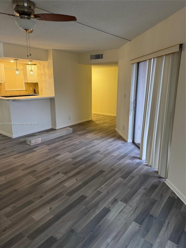 unfurnished living room featuring dark wood-style flooring, visible vents, a textured ceiling, and baseboards