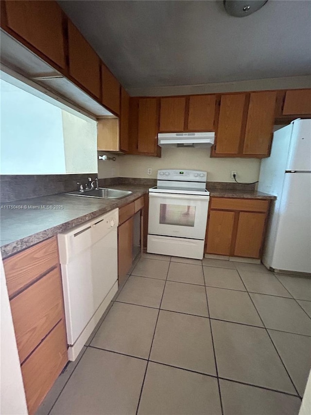 kitchen with light tile patterned floors, under cabinet range hood, white appliances, a sink, and brown cabinetry