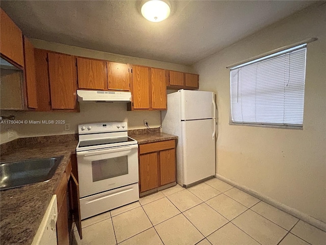 kitchen featuring light tile patterned floors, under cabinet range hood, white appliances, brown cabinets, and dark countertops