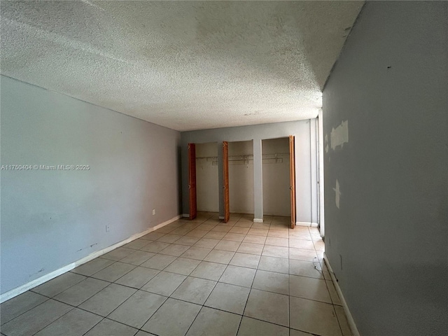 unfurnished bedroom with light tile patterned floors, a textured ceiling, two closets, and baseboards