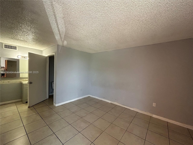 spare room with light tile patterned floors, a textured ceiling, visible vents, and baseboards