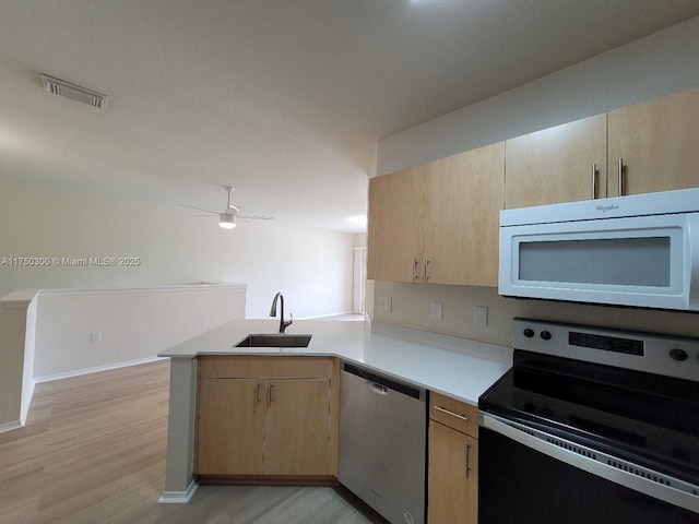 kitchen with a peninsula, appliances with stainless steel finishes, a sink, and light brown cabinetry