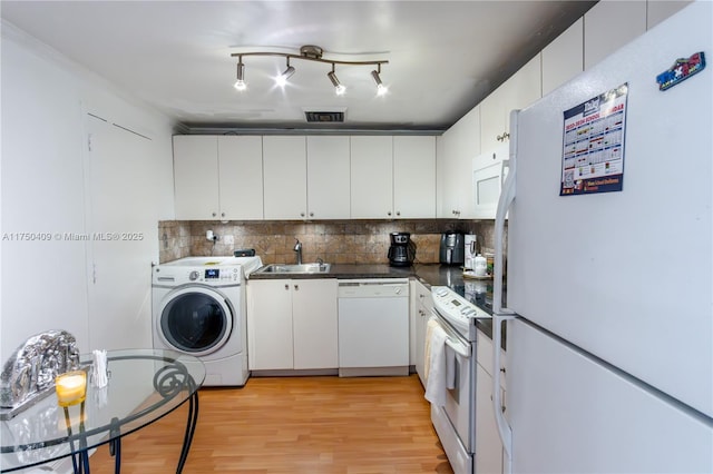 kitchen with white appliances, a sink, white cabinetry, dark countertops, and washer / dryer