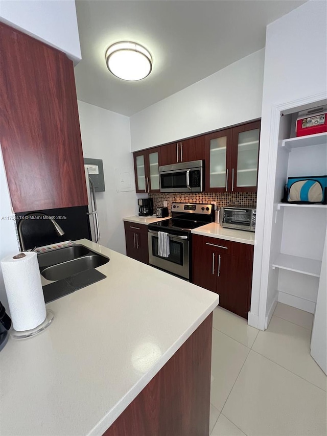 kitchen with stainless steel appliances, a sink, light countertops, backsplash, and glass insert cabinets