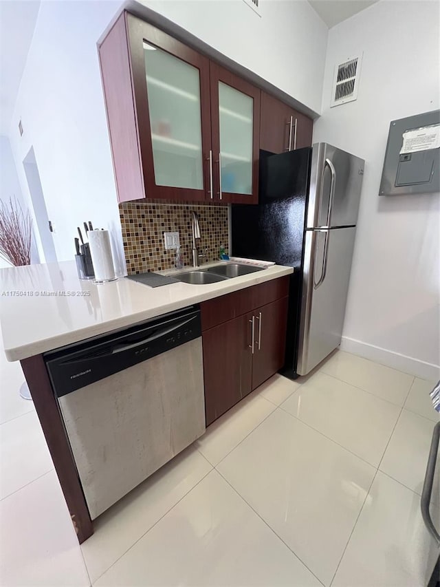 kitchen featuring a sink, light countertops, appliances with stainless steel finishes, backsplash, and glass insert cabinets