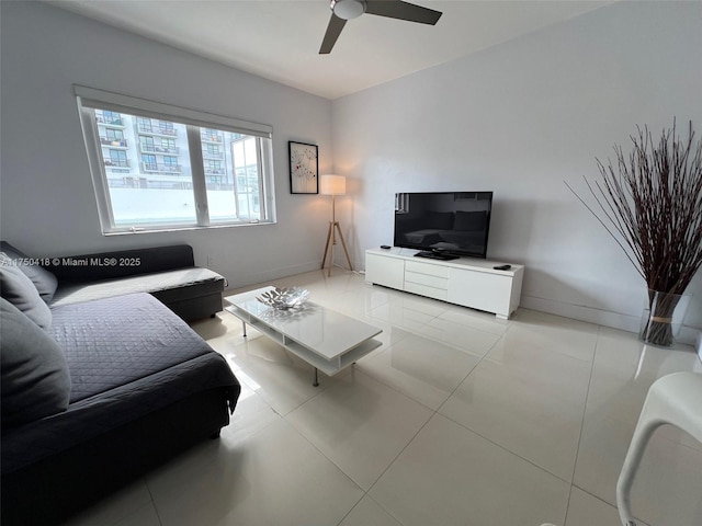 living area with a ceiling fan, light tile patterned flooring, and baseboards