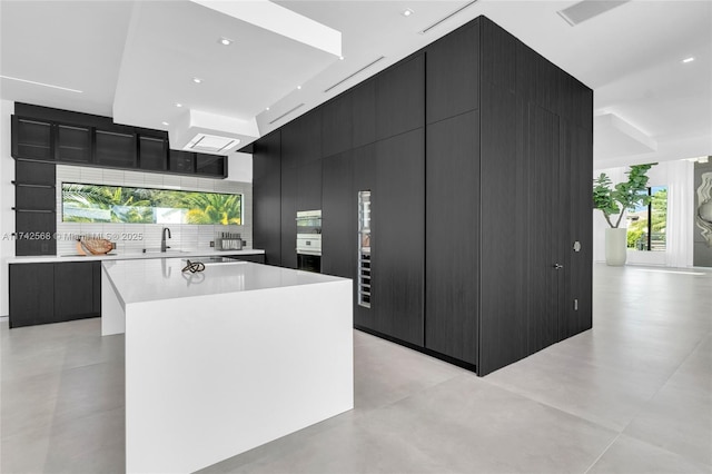 kitchen with a spacious island, light countertops, dark cabinetry, backsplash, and modern cabinets