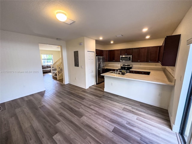 kitchen with electric panel, wood finished floors, a peninsula, stainless steel appliances, and light countertops