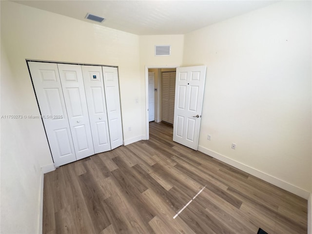 unfurnished bedroom featuring baseboards, a closet, visible vents, and wood finished floors