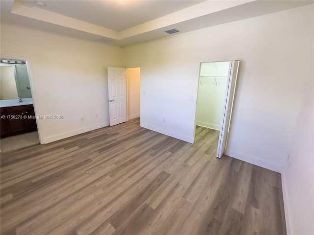 unfurnished bedroom with a tray ceiling, baseboards, and wood finished floors