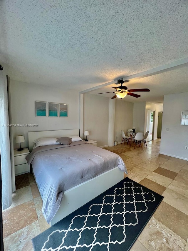 bedroom featuring a ceiling fan, stone finish floor, a textured ceiling, and baseboards