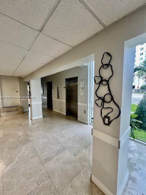 interior space with a paneled ceiling, elevator, and baseboards