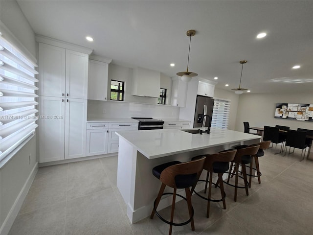 kitchen featuring a breakfast bar, a center island with sink, white cabinets, and light countertops