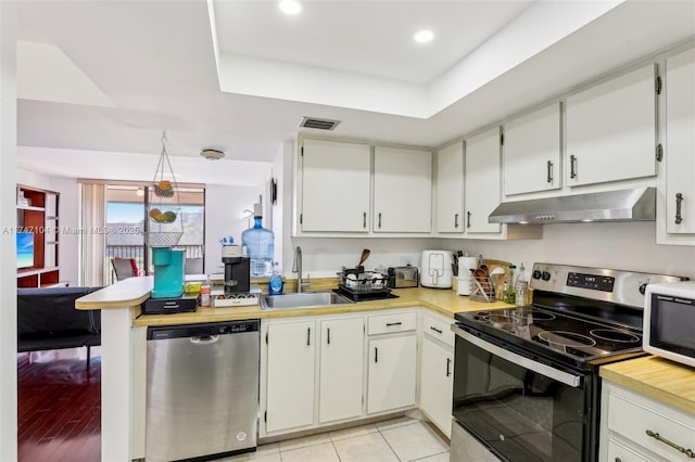 kitchen with white cabinets, stainless steel appliances, light countertops, under cabinet range hood, and a sink