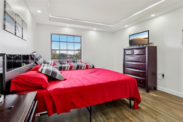 bedroom featuring baseboards, a raised ceiling, wood finished floors, and recessed lighting