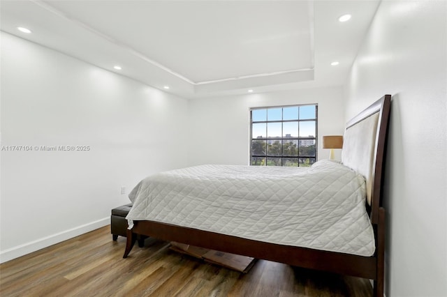 bedroom featuring baseboards, a raised ceiling, wood finished floors, and recessed lighting