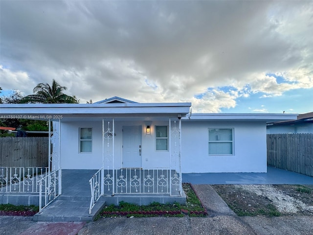 view of front facade with a porch, fence, and stucco siding