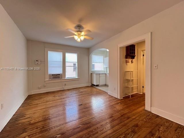 spare room with arched walkways, dark wood-style flooring, ceiling fan, cooling unit, and baseboards