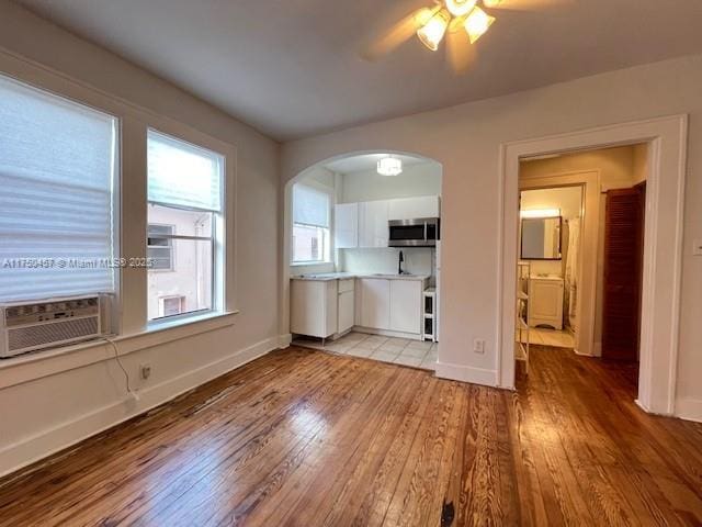 interior space with arched walkways, stainless steel microwave, light countertops, light wood-type flooring, and white cabinetry