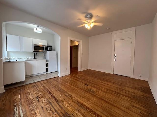 unfurnished living room featuring arched walkways, ceiling fan, light wood finished floors, and a sink