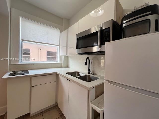 kitchen featuring light countertops, stainless steel microwave, freestanding refrigerator, white cabinets, and a sink