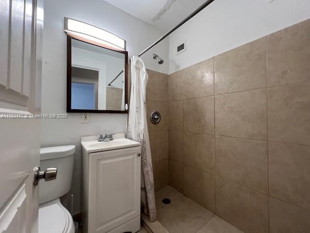 full bathroom featuring visible vents, tiled shower, vanity, and toilet