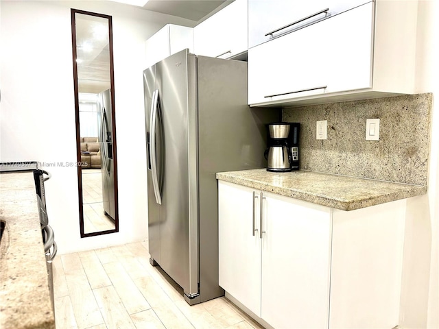 kitchen featuring white cabinets, stainless steel fridge with ice dispenser, light stone countertops, light wood-type flooring, and backsplash