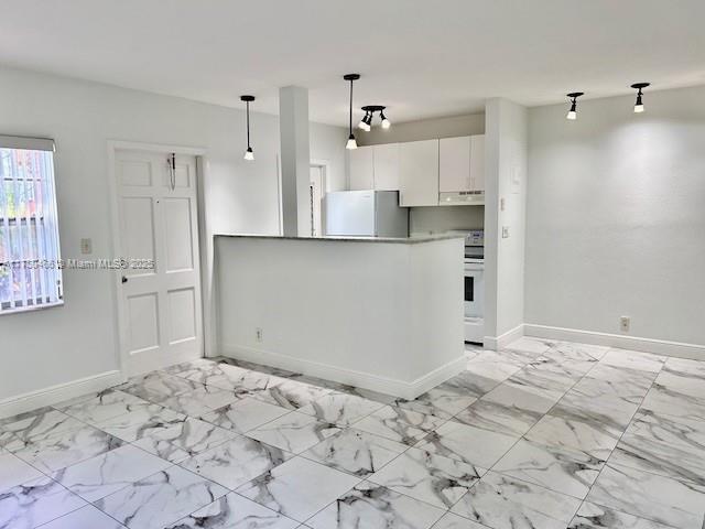 kitchen featuring baseboards, white cabinets, hanging light fixtures, range, and freestanding refrigerator