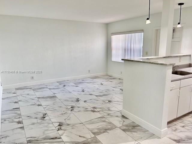 kitchen with pendant lighting, white cabinetry, marble finish floor, and baseboards