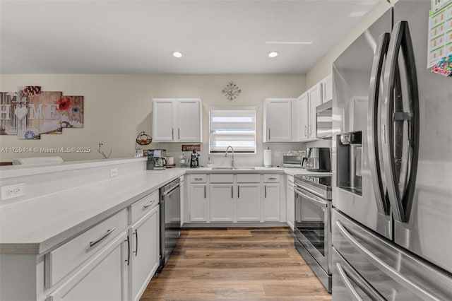 kitchen with light countertops, appliances with stainless steel finishes, white cabinets, a sink, and a peninsula