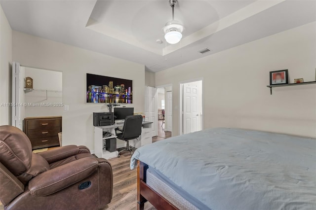 bedroom featuring light wood-style floors, visible vents, and a raised ceiling