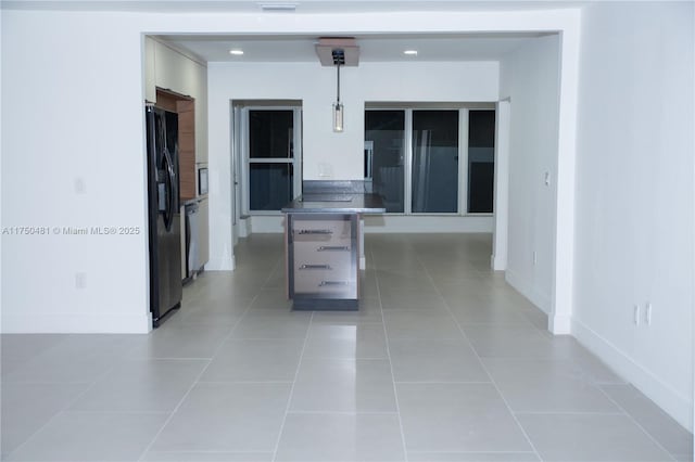 kitchen featuring light tile patterned floors, baseboards, dark countertops, freestanding refrigerator, and decorative light fixtures