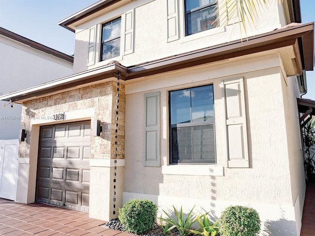 view of exterior entry featuring stone siding, decorative driveway, and stucco siding