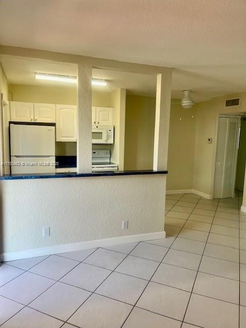 kitchen with light tile patterned flooring, white appliances, visible vents, baseboards, and white cabinets