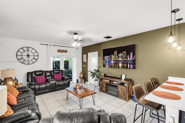 living room with light tile patterned floors, ceiling fan, a glass covered fireplace, and visible vents