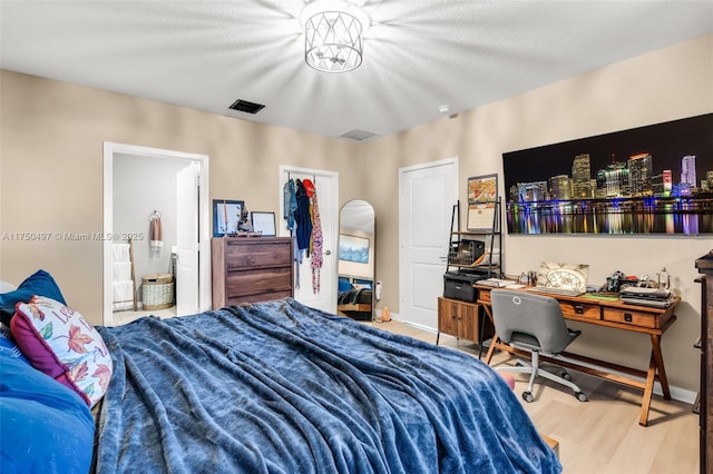 bedroom with a walk in closet, visible vents, light wood-style flooring, and baseboards