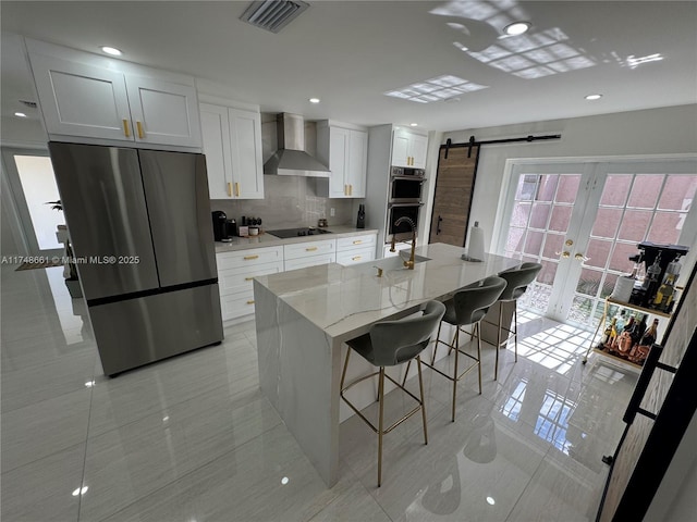 kitchen with a kitchen island with sink, a breakfast bar, white cabinets, wall chimney range hood, and appliances with stainless steel finishes