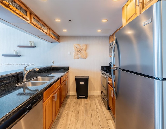 kitchen with stainless steel appliances, brown cabinetry, dark stone countertops, and a sink