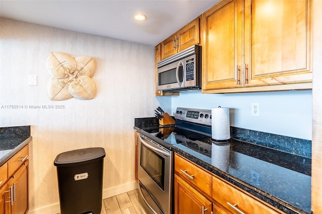 kitchen with light wood-type flooring, appliances with stainless steel finishes, brown cabinets, and dark stone counters