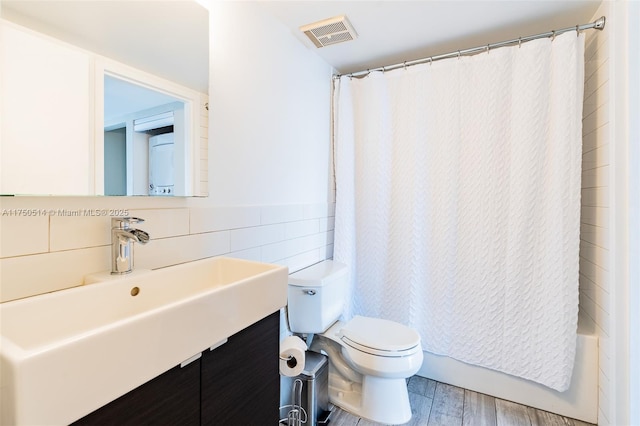 bathroom featuring visible vents, toilet, wood finished floors, vanity, and tile walls