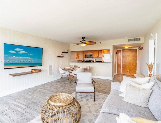 living room with light wood-type flooring, ceiling fan, visible vents, and baseboards