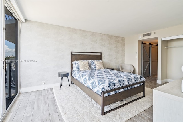 bedroom with a barn door, wood finished floors, visible vents, access to exterior, and baseboards