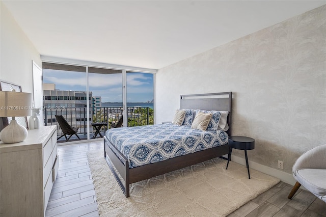 bedroom featuring light wood-type flooring, access to outside, expansive windows, and baseboards